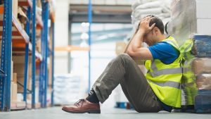 A warehouse worker sat down holding is head in his hands